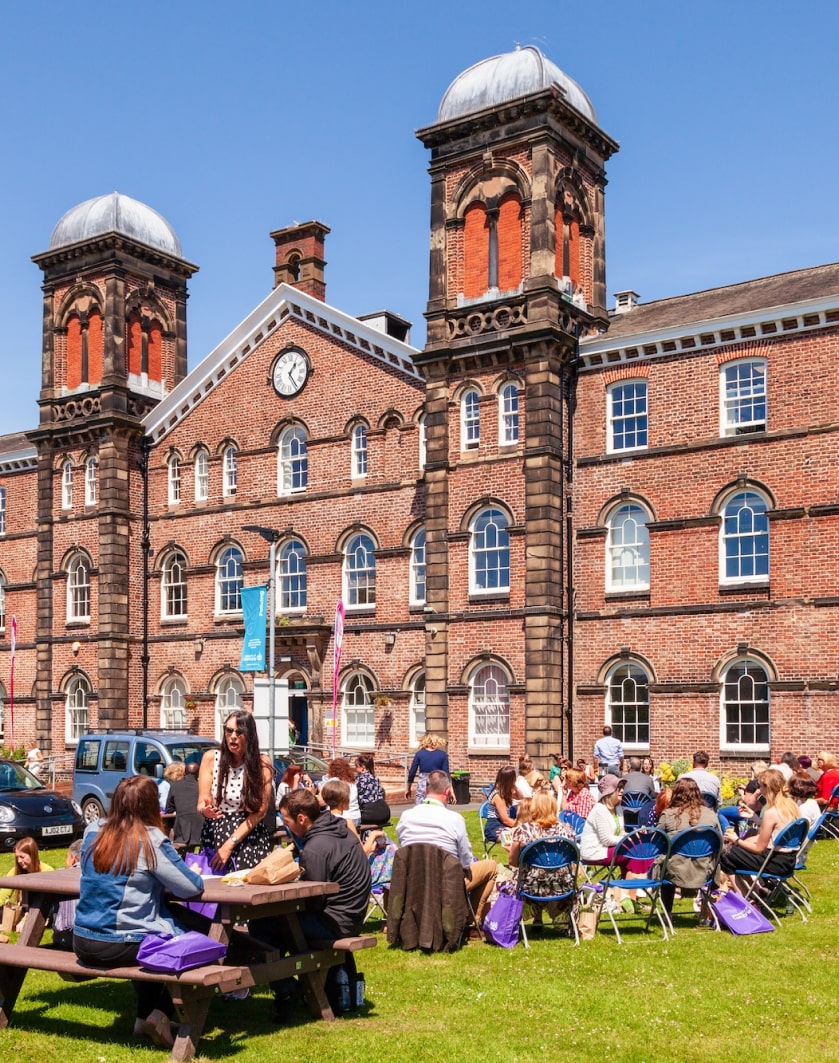 People sitting at tables in front of a brick building.