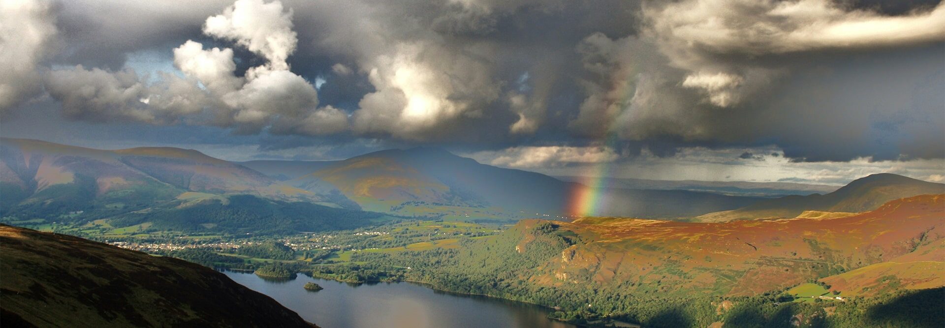 A rainbow is seen over a lake and mountains.