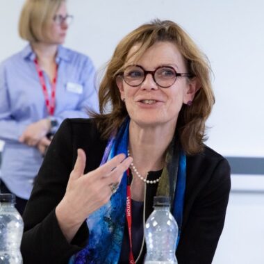 A woman in glasses is speaking at a meeting.