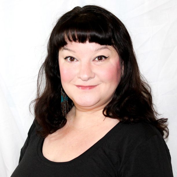 Woman with dark hair and bangs, wearing a black top, poses against a white background.