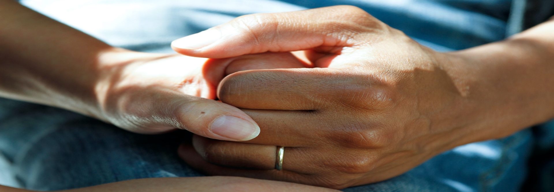 Two hands clasped together, one adorned with a gold ring, rest gently on a blue fabric background, symbolizing unity and support championed by the Pears Foundation.